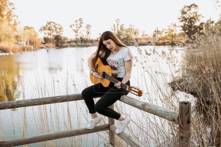 Photo for Young woman playing guitar near water - Royalty Free Image