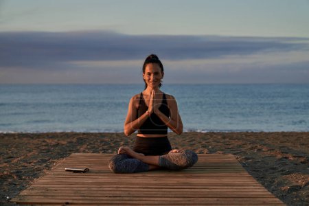 Photo for Full body of optimistic barefoot Hispanic female looking away with smile while meditating on coast near sea during yoga session - Royalty Free Image