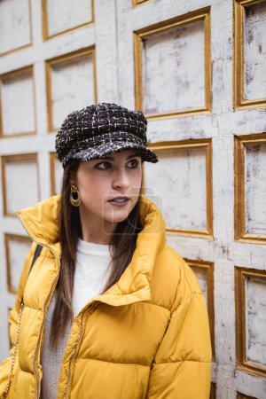 Photo for Pretty young female in trendy outfit looking away while standing near weathered wall on city street - Royalty Free Image