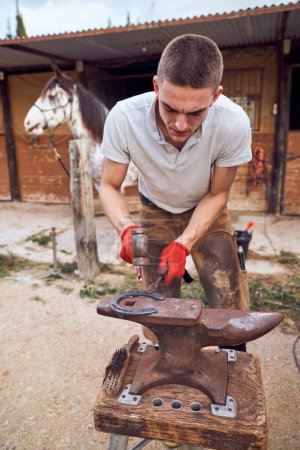 Photo for Blacksmith boy working on the anvil changing the horseshoe to a leg with tools - Royalty Free Image