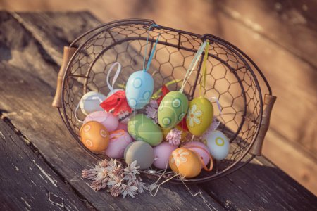 Téléchargez les photos : Œufs de Pâques colorés dans le panier avec bouquet de fleurs sur fond flou à la lumière vive - en image libre de droit