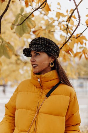 Photo for Beautiful young lady in stylish warm clothes smiling and standing on tree on amazing autumn day on city street - Royalty Free Image