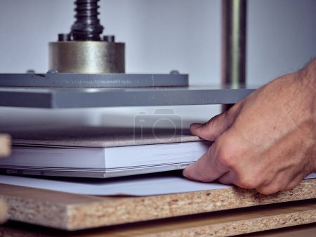 Photo for Crop anonymous craftsman placing new hardcover book under press machine while working in creative workshop - Royalty Free Image