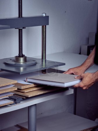 Foto de Manos de hombre irreconocible trabajando poniendo libro en la máquina de prensa encuadernador en la mesa en el taller - Imagen libre de derechos