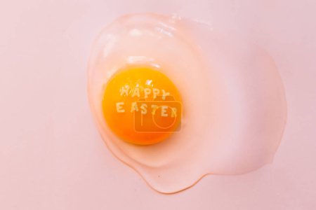 Photo for From above raw broken egg with text Happy Easter on yellow yolk on pink background - Royalty Free Image