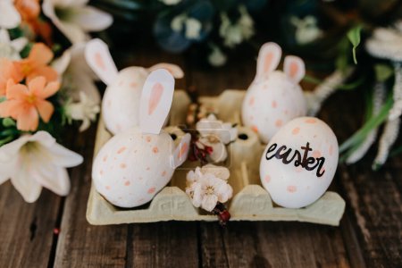 Photo for Easter eggs with rabbit ears painted by children in an egg cup with flowers - Royalty Free Image