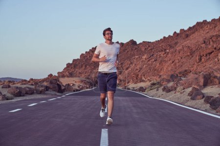 Photo for Full body of active male runner in activewear running on asphalt highway near rocky mountain range in nature on summer day - Royalty Free Image