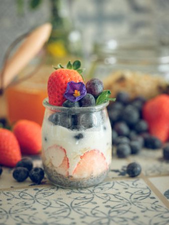 Photo for Fresh yogurt with ripe strawberries and blueberries in glass jar placed on table in rustic kitchen - Royalty Free Image