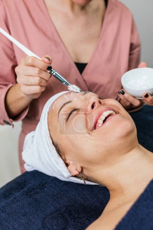 Photo for Cropped unrecognizable cosmetologist applying moisturizing facial mask on face of female customer during skincare procedure in modern beauty salon - Royalty Free Image