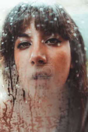 Schöne Frau atmet auf nasser Oberfläche aus transparentem Glas und schaut in die Kamera