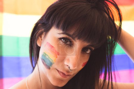 Foto de Hermosa mujer joven seria con dibujo LGBT en la cara mirando a la cámara en el fondo de tela LGBT - Imagen libre de derechos