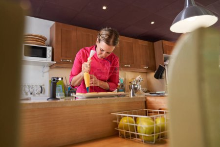 Téléchargez les photos : Chef pâtissier femme faisant des pics de crème sur les tartelettes tout en se tenant dans la cuisine de la boulangerie maison - en image libre de droit