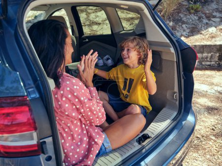 Foto de Sonriente hijo mirando a la madre mientras juega Pat un juego de pastel en el maletero del automóvil estacionado en el campo en el día de verano - Imagen libre de derechos
