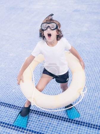 Photo for From above full length of cheerful kid with open mouth wearing snorkeling mask and flippers holding inflatable ring while standing on bottom of empty pool - Royalty Free Image