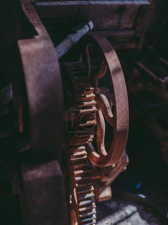 Téléchargez les photos : Gros plan de machine métallique rouillée âgée avec roue rotative ronde placée dans une usine industrielle abandonnée sombre - en image libre de droit