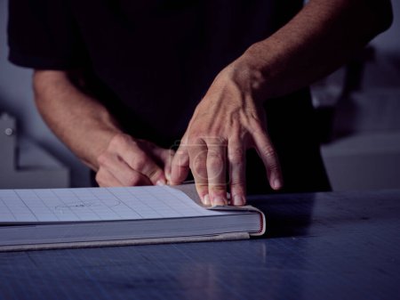 Foto de Artesano de cosecha irreconocible de pie en la mesa y presionando tela pegada al cartón mientras hace la cubierta del libro en el taller de encuadernación - Imagen libre de derechos