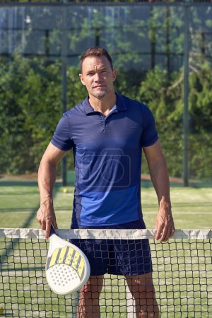 Photo for Active male in sportswear with racket looking at camera while standing near net during padel training on sunny summer day - Royalty Free Image