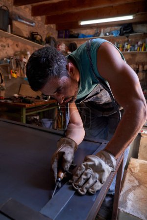 Téléchargez les photos : Artisanat masculin concentré en vêtements de travail debout sur l'établi et mesurant la tôle tout en faisant du travail des métaux dans un atelier professionnel - en image libre de droit