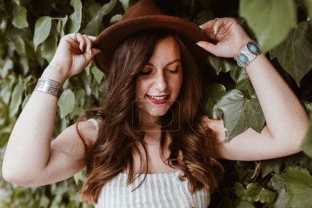 Photo for Attractive long haired happy woman in hat in the middle of green leaves - Royalty Free Image