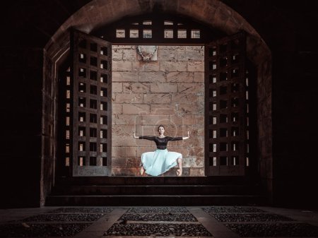 Foto de Cuerpo completo de elegante bailarina sentada en plie en zapatos puntiagudos cerca de la pared de ladrillo del viejo castillo - Imagen libre de derechos