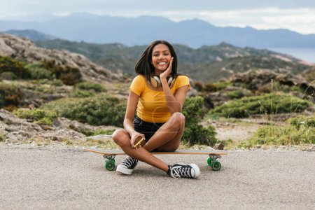 Téléchargez les photos : Ethnique femelle assis longboard sur asphalte route - en image libre de droit