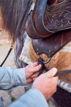 Téléchargez les photos : Un homme place une selle sur un cheval - en image libre de droit