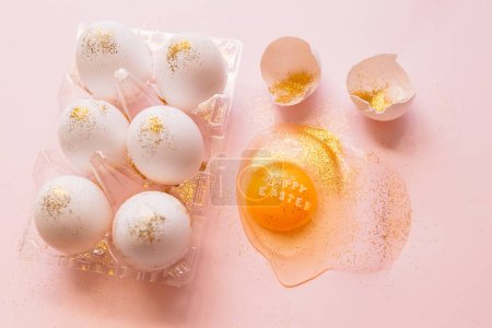 Photo for Top view of broken glittered egg with text Happy Easter and raw eggs in plastic box on pink background - Royalty Free Image