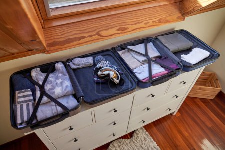 Téléchargez les photos : D'en haut des valises ouvertes avec des vêtements chauds à l'intérieur placés sur une armoire en bois près de la fenêtre tout en se préparant pour le voyage - en image libre de droit