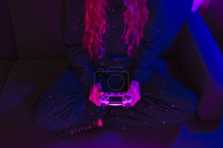 Téléchargez les photos : Vue de face d'une fille blonde avec une manette de jeu vidéo et des lumières colorées - en image libre de droit