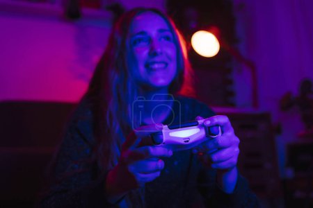 Téléchargez les photos : Vue rapprochée d'une fille heureuse jouant à des jeux vidéo avec des lumières colorées dans un salon pendant le confinement de Corona. - en image libre de droit