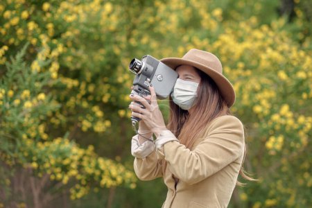 Téléchargez les photos : Photographe masqué marchant dans le parc avec caméra vidéo vintage - en image libre de droit