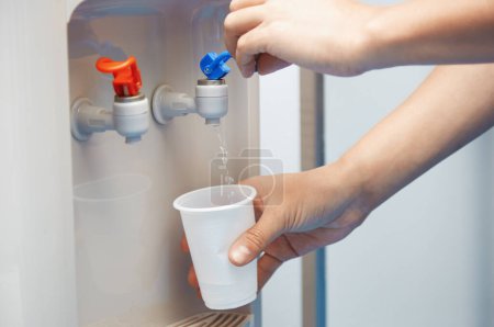 Téléchargez les photos : Homme remplissant la tasse en plastique au refroidisseur d'eau - en image libre de droit