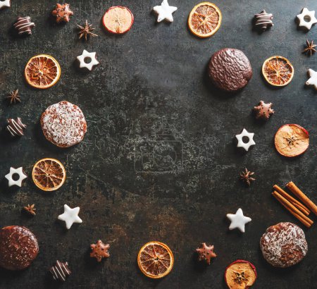Frame with seasonal Christmas sweets and flavorful spices: cookies and gingerbread, dried orange slices, cinnamon and star anise on dark background. Top view with copy space. Flat lay