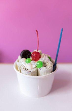 Photo for Close up of a rolled ice cream decorated with a cherry, a cookie and green bubble toppings. Concept of new small business - Royalty Free Image