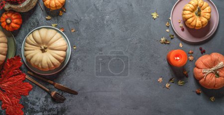 Téléchargez les photos : Vue de dessus du cadre de fond d'automne avec diverses citrouilles, feuilles d'automne rouges, assiettes, couverts et bougie en toile de fond gris foncé - en image libre de droit