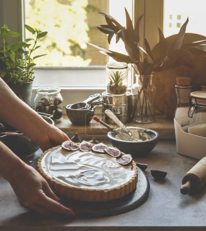 Photo for Woman hand holding homemade cheesecake with figs at kitchen background with window and natural light. Baking delicious cake at home with fruit and cream. Front view. - Royalty Free Image