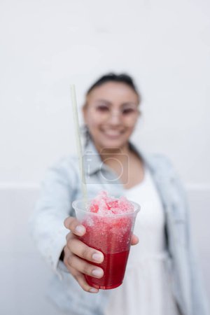Téléchargez les photos : Une jeune femme hispanique sourit en buvant une bouillie de cerises mexicaine à l'extérieur. Concept de boisson estivale - en image libre de droit