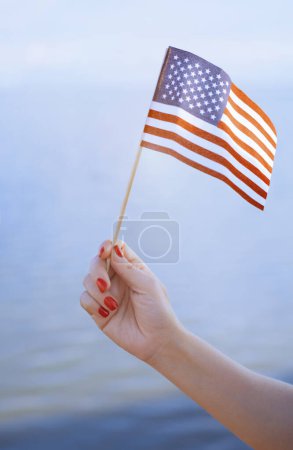 Photo for Woman hand holding USA flag in front of the ocean - Royalty Free Image