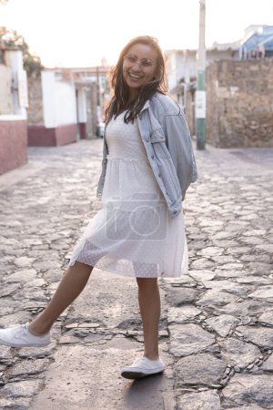 Foto de Una joven hispana con gafas de sol está sonriendo posando en la calle durante el atardecer. Concepto de estilo de vida al aire libre sesión de fotos - Imagen libre de derechos