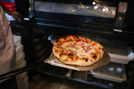 Foto de Pizza napolitana recién sacada del horno con una pala por un pizzero irreconocible en una pizzería - Imagen libre de derechos