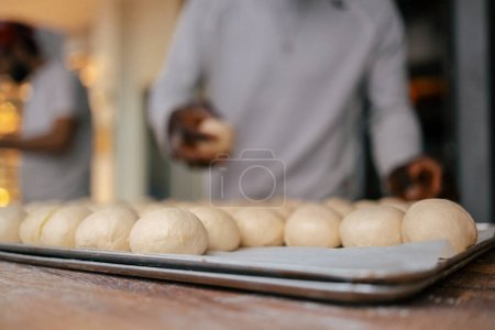 Foto de Detalle de cerca de bolitas de masa en una bandeja con un panadero en el fondo en una panadería - Imagen libre de derechos