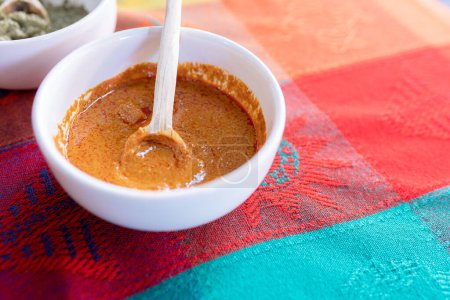 Téléchargez les photos : Un bol de sauce jaune taupe avec une cuillère en bois sur le dessus d'une nappe traditionnelle colorée. Concept de nourriture mexicaine - en image libre de droit