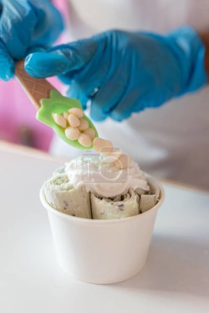 Photo for A worker is decorating a rolled ice cream tub with yogurt bubble toppings on top with a spoon. Concept of new small business - Royalty Free Image