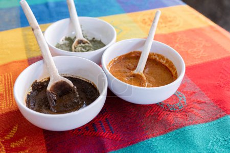 Foto de Tres cuencos con salsa mole roja, verde y amarilla con una cuchara de madera encima de un mantel tradicional colorido. Concepto de comida tradicional mexicana de Puebla y Oaxaca - Imagen libre de derechos
