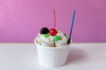 Photo for Close up of a rolled ice cream decorated with a cherry, a cookie and green bubble toppings. Concept of new small business - Royalty Free Image