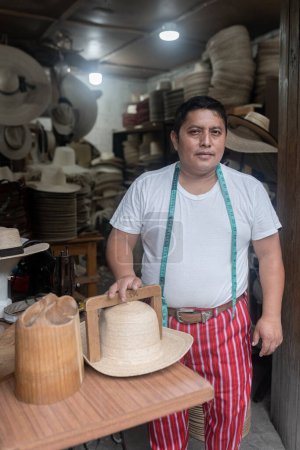 Porträt eines erwachsenen hispanischen Schneiders, der mit Hut in seiner Werkstatt in Guatemala posiert