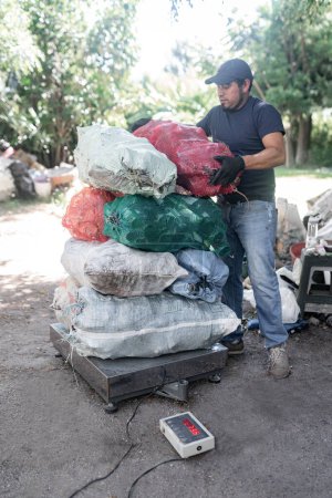 Foto de Hombre hispano adulto pesa meticulosamente una pila sustancial de botellas de cristal reciclado, lo que ilustra la implicación dedicada en el cuidado del medio ambiente - Imagen libre de derechos