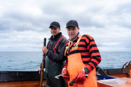 Zwei Fischer blicken während der Arbeit an einem Hummerfischerboot in die Kamera