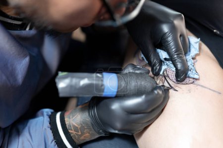 Téléchargez les photos : Un tatoueur tatoue un serpent sur la jambe d'une femme. Ferme là. Concept de studio de tatouage - en image libre de droit
