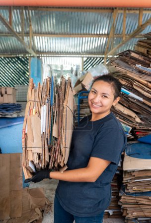 A young Hispanic woman stands in a portrait while holding a heavy Stack of cardboard, symbolizing her commitment to responsible recycling practices